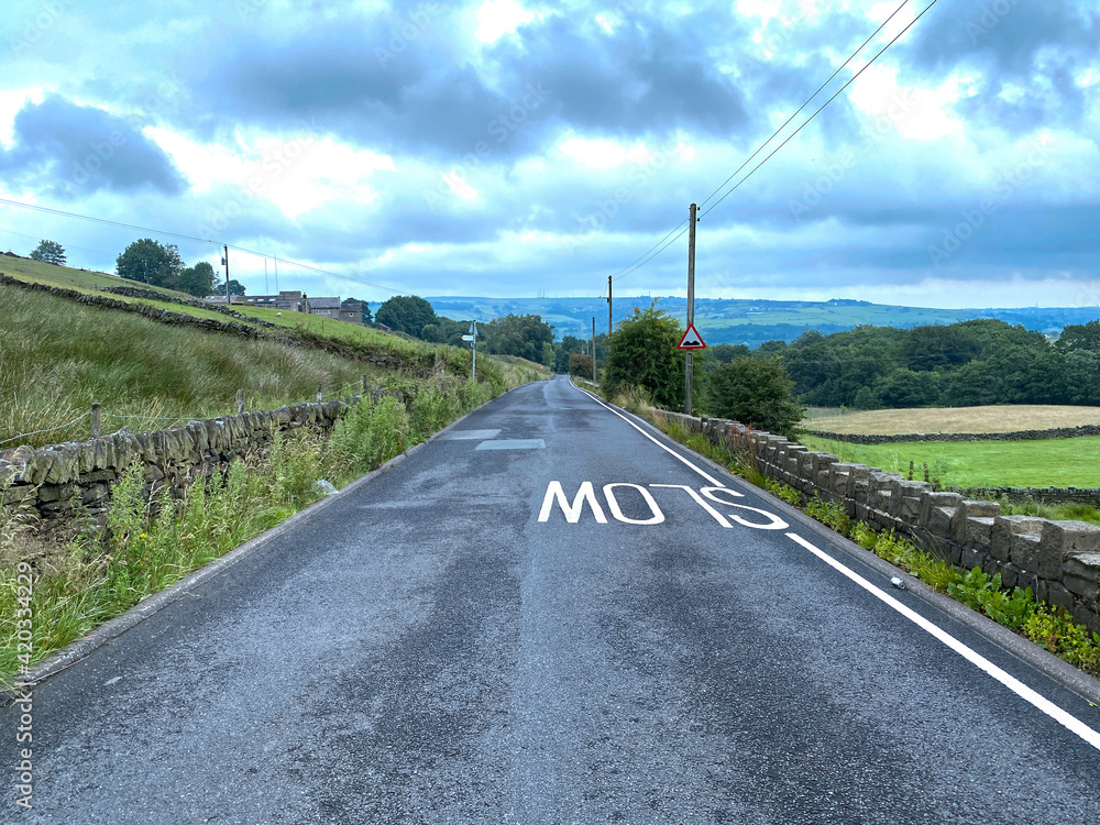 Fototapeta premium View down, Varley Road, with dry stone walls, fields and distant hills in, Slaithwaite, Huddersfield, UK