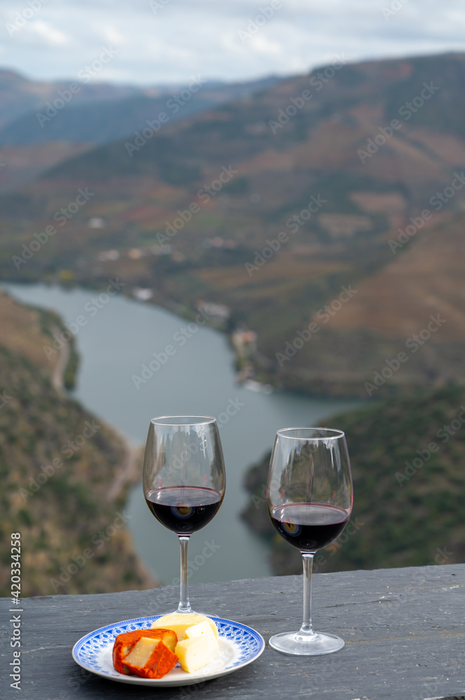 Tasting of Portuguese red dry wine, produced in Douro Valley with goat and sheep cheese and Douro river and terraced vineyards on background in autumn, Portugal