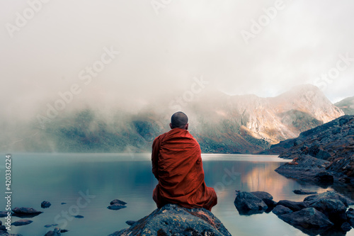 Fototapeta Tibetan monk from back sitting on the stone near the water in the background of