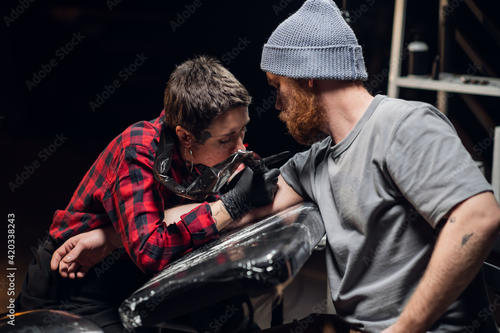 To the client of the tattoo salon, a young girl artist makes a painless tattoo on her arm using the stick and poke method To the client of the tattoo salon, a young girl artist makes a painless tattoo on her arm using the stick and poke method
