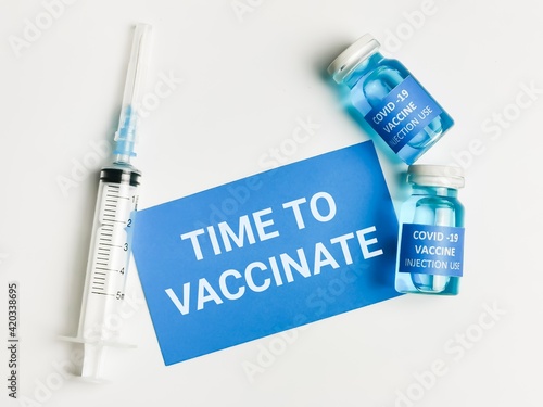 Phrase TIME TO VACCINATE written on blue card with two bottles vaccine and syringe.