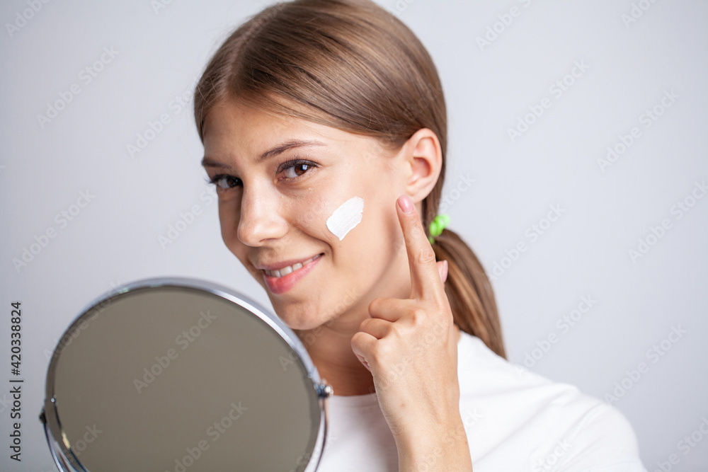 Beautiful young woman applying moisturizer cream onto her face Beautiful young woman applying moisturizer cream onto her face