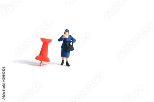 Miniature people toys conceptual photography. Courier pinpoint location pickup package delivery service. Postman with red push pin, isolated white background.