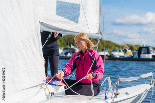 Two young female athletes prepare a sailing boat for the regatta on the river pier.