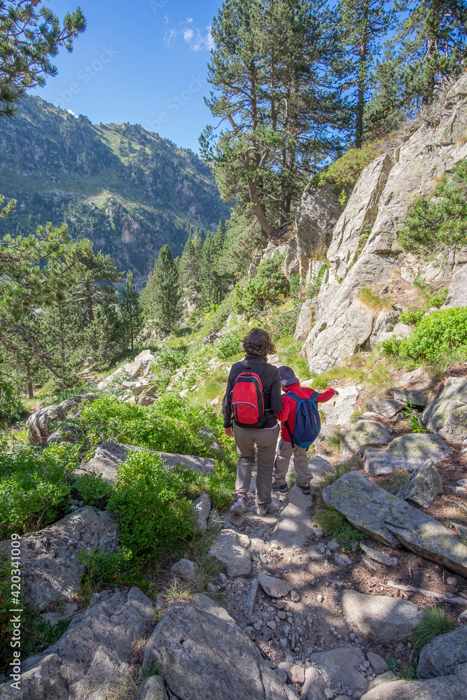 mother and son walk down a mountain trail hand in hand with backpacks and mountain clothing, vertical