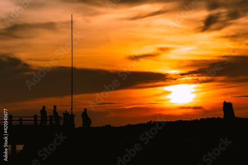 Silhouette of people enjoying nice warm sunset at the edge of the bridge