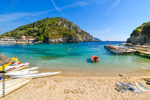 Boats in the clear aqua blue water at the sandy beach of Palaiokastritsa on the Aegean island of Corfu, Greece.