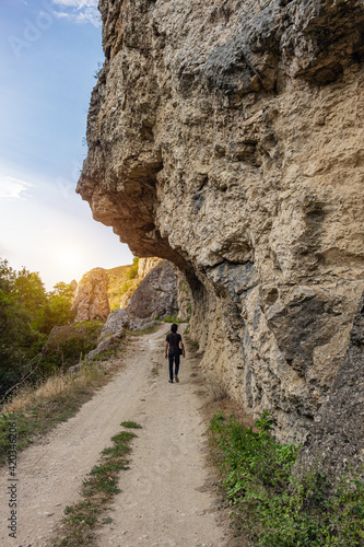 Lonely man, tourist or hiker walking on a pathway under the beautiful rock formation. View from behind, vertical image.