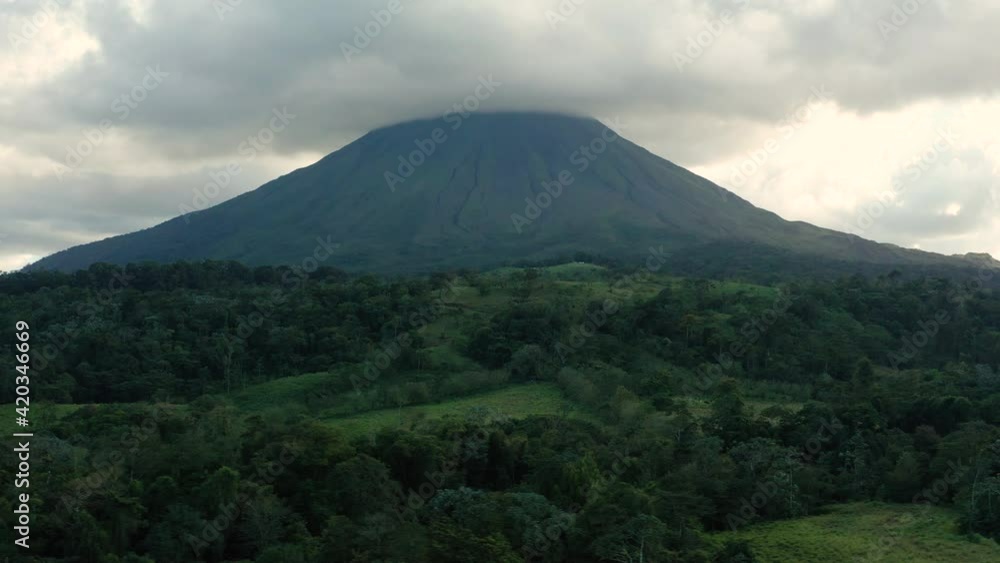 Drone pans sideways across pasture and rainforest with Arenal volcano looming nearby Drone pans sideways across pasture and rainforest with Arenal volcano looming nearby