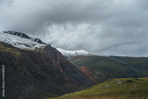 Atmospheric alpine landscape with deep gorge and snow-capped multicolor mountains in overcast weather. Beautiful scenery with snowbound mountain range under cloudy sky. Motley high mountains with snow