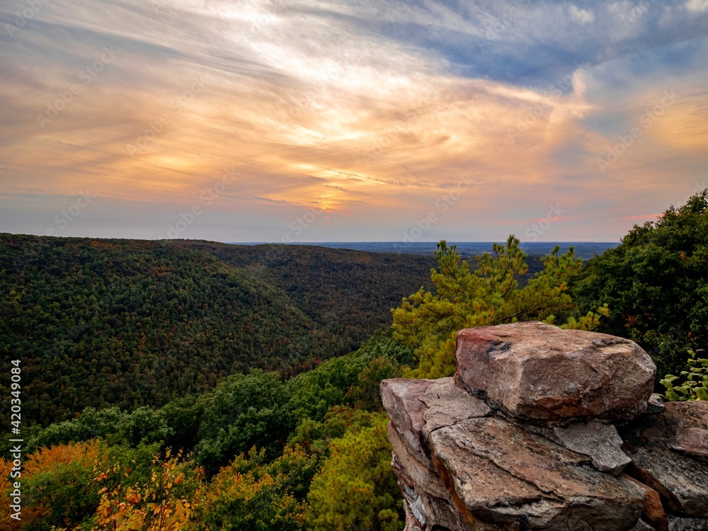 Fototapeta premium Overlook of the mountains and the fall foliage at Coopers Rock State Forest in West Virginia with the sunset golden sky one direction and a blue swirly sky the other direction, with the rock cliff.
