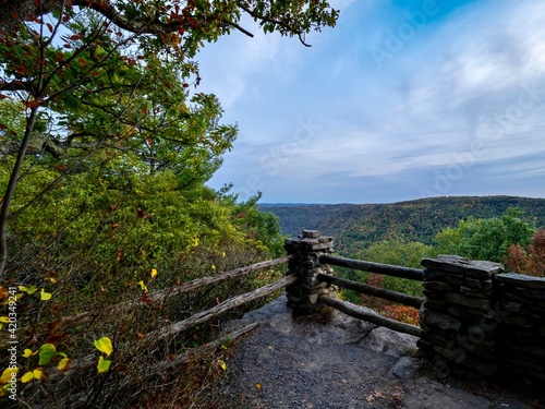 Overlook of the mountains and the fall foliage at Coopers Rock State Forest in West Virginia with the sunset golden sky one direction and a blue swirly sky the other direction  with the rock cliff.