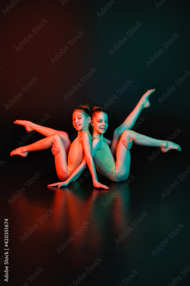 Two young gymnasts in a pose on a black background with neon lighting mixed light.