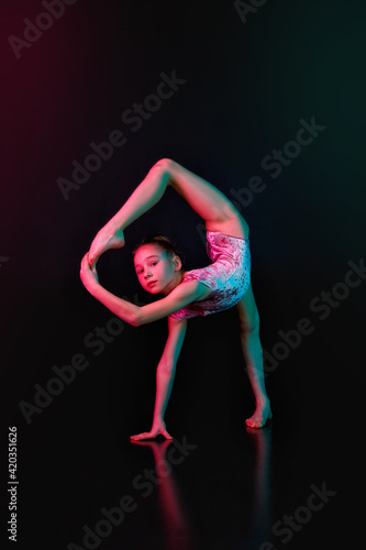 Balance. A girl is a young athlete  a gymnast in a pose in isolation on a black studio background in neon mixed color light.