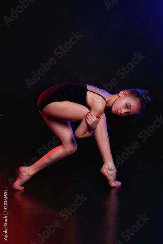 Balance. A girl is a young athlete, a gymnast in a pose in isolation on a black studio background in neon mixed color light.