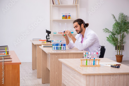 Young male chemist sitting at the desk in the classroom