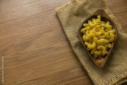 Raw and uncooked elbow macaroni on wooden bowl on wooden background with copy space.