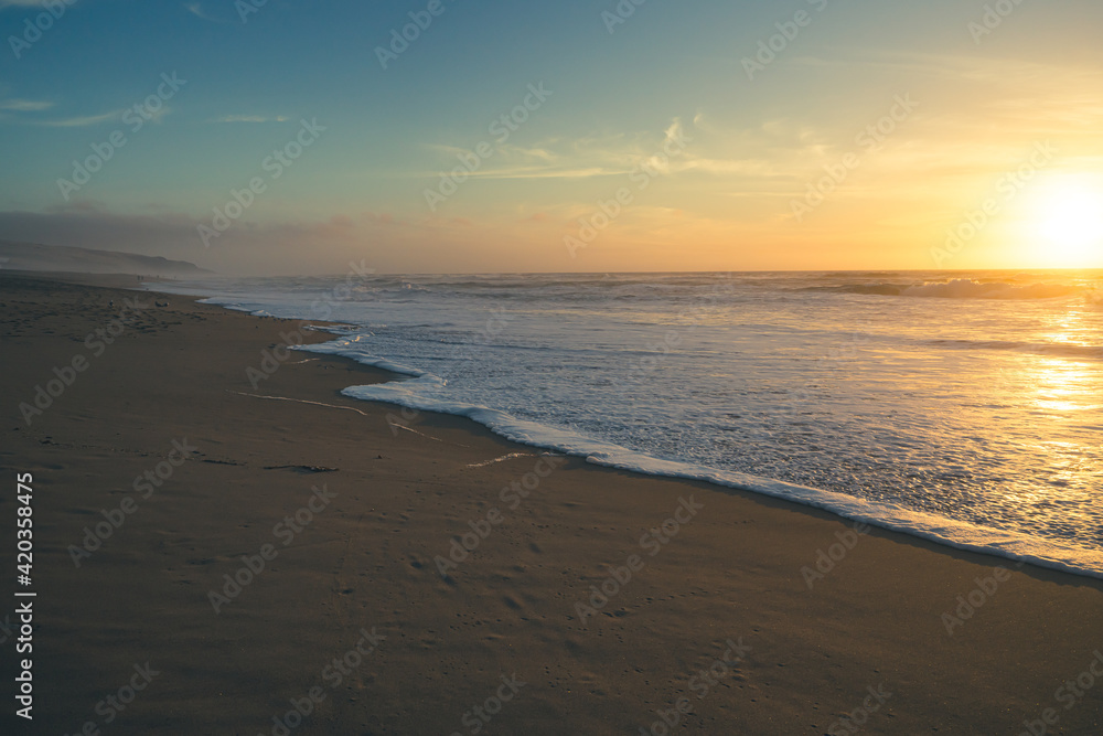 Beach sunset. Empty sand beach, sea waves, and sun setting down the horizon. Tranquil, calm scene, soft focus, copy space