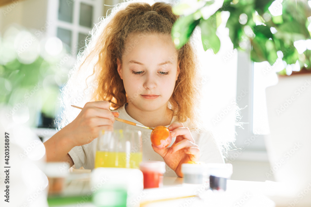 Cute tween girl with long curly hair painting eggs on kitchen at home on spring sunny day, Happy Easter Cute tween girl with long curly hair painting eggs on kitchen at home on spring sunny day, Happy Easter