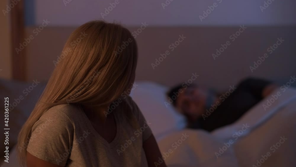 Couple issue. Night insomnia. Relationship problem. Anxious disturbed woman sitting on in bedroom with sleeping husband behind her. Couple issue. Night insomnia. Relationship problem. Anxious disturbed woman sitting on in bedroom with sleeping husband behind her.