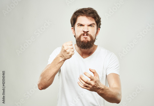 Indignant man in a white T-shirt gesturing with his hands on a light background cropped view