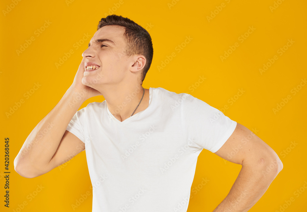 A man in a white T-shirt touches his face with his hand on a yellow background of emotion A man in a white T-shirt touches his face with his hand on a yellow background of emotion