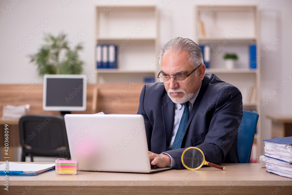 Old male employee auditor holding loupe at workplace Old male employee auditor holding loupe at workplace
