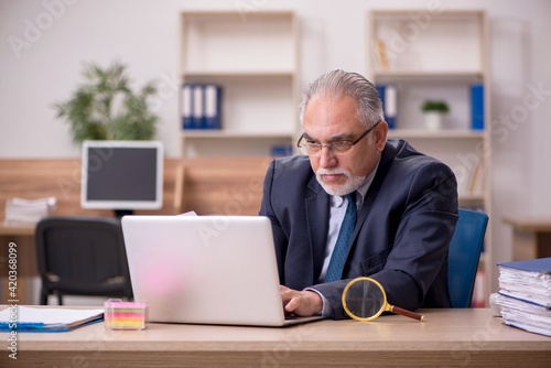 Wallpaper Mural Old male employee auditor holding loupe at workplace Torontodigital.ca