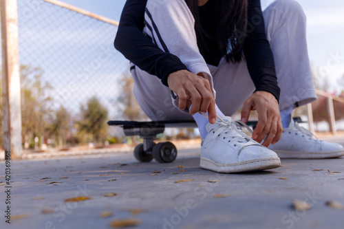 Young women sitting on a surf skate board tying a shoe before play. Young girl long hair sitting and tying a sneaker at public park on morning before play surf skate board