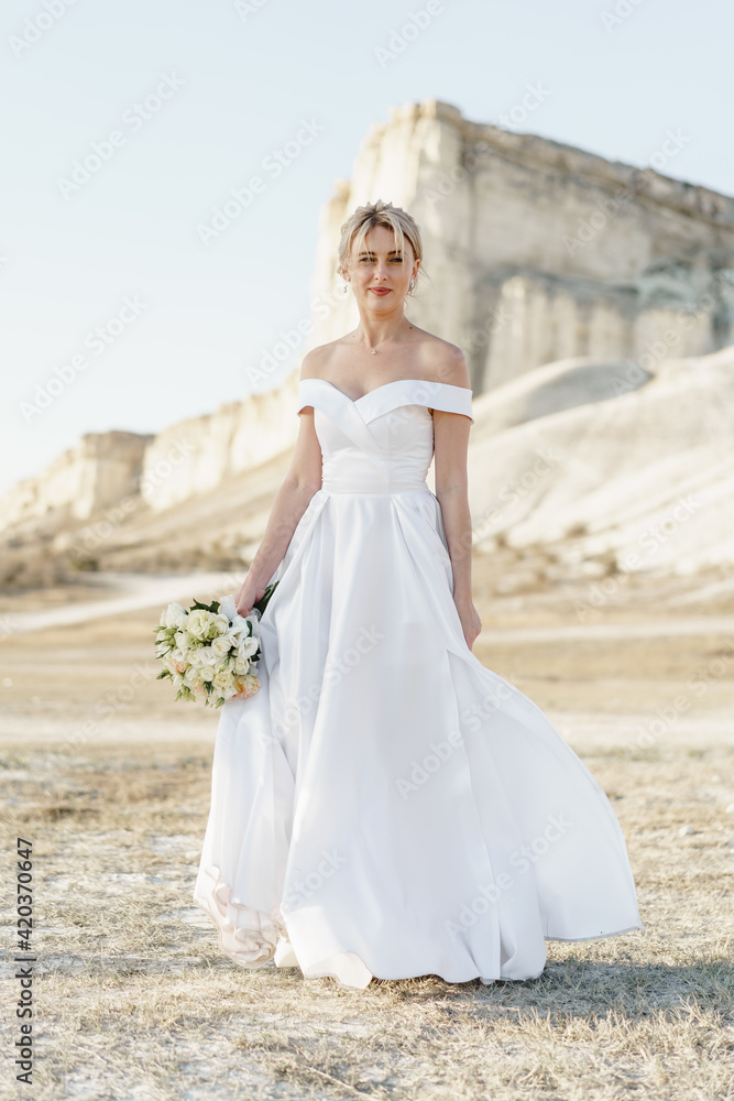 Beautiful bride in a wedding dress with a bouquet standing against white rock