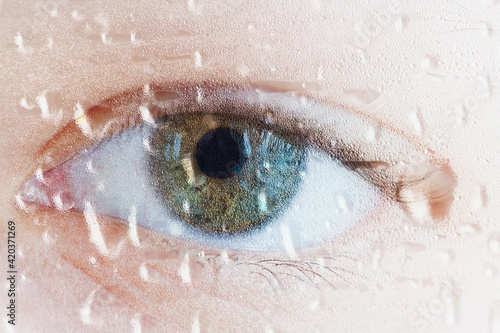 Human eye through wet glass. Water drops, sadness and sadness concept. Focusing on water droplets.