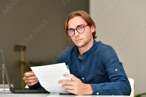 young man wearing glasses holding a credit card and some bills while looking at the camera