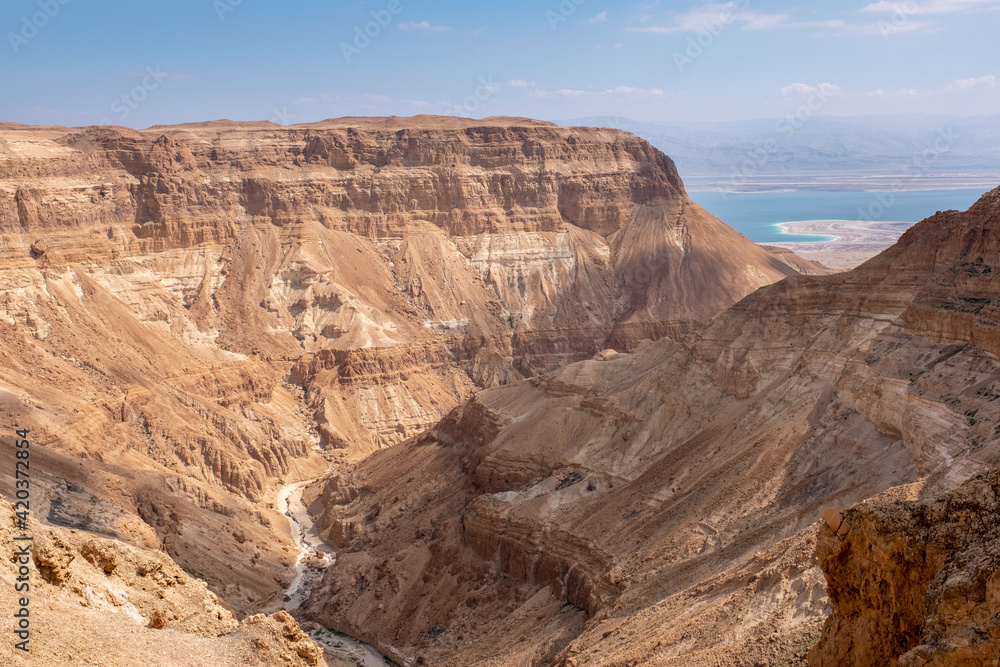 A picturesque view on a dry wadi Hever in the nature reserve in Judaean Desert. Typical landscape with a dry wadi bend and high mountain slopes in the desert. Dead Sea on the background.