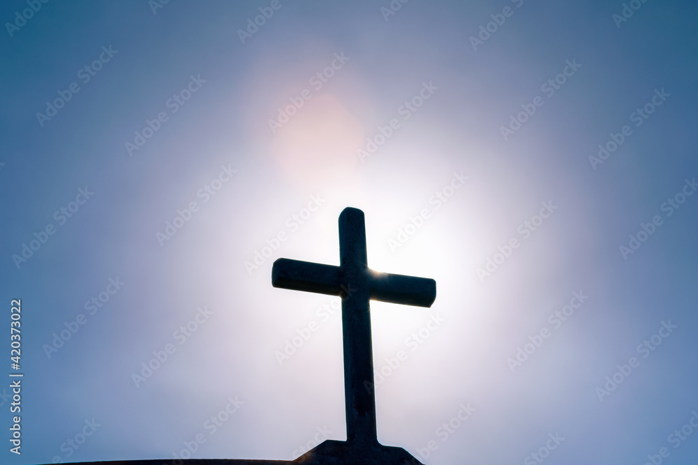 Crucifixion of Jesus Christ, silhouette of an old metal cross, church spire against the background of a dramatic sky with a bright ray of the sun, Ascension day concept, Easter morning