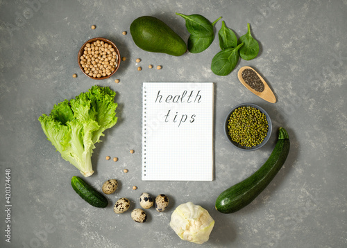 Health tips in a notebook on a gray table with a vegetable composition of zucchini, chickpeas, lentils and quail eggs