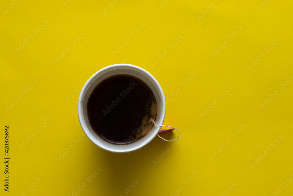 A disposable white cup full of tea, yellow background - obrazy, fototapety, plakaty 