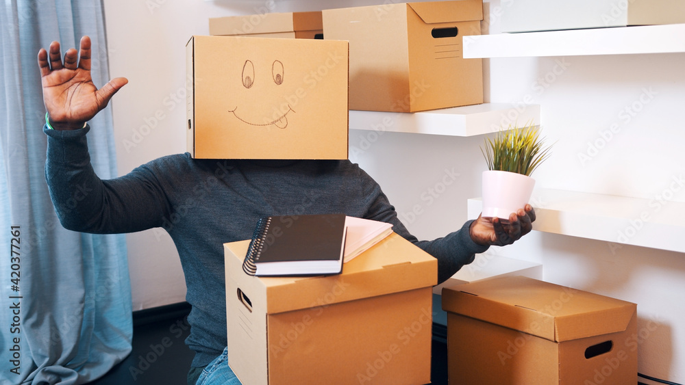 Fototapeta premium Unrecognizable black man with cardboard box on the head dancing in new apartment. High quality photo