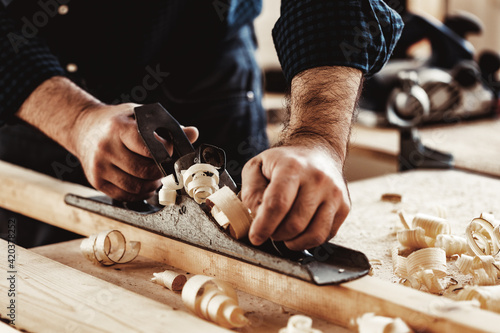 Carpenter's hands planing a plank of wood with a hand plane