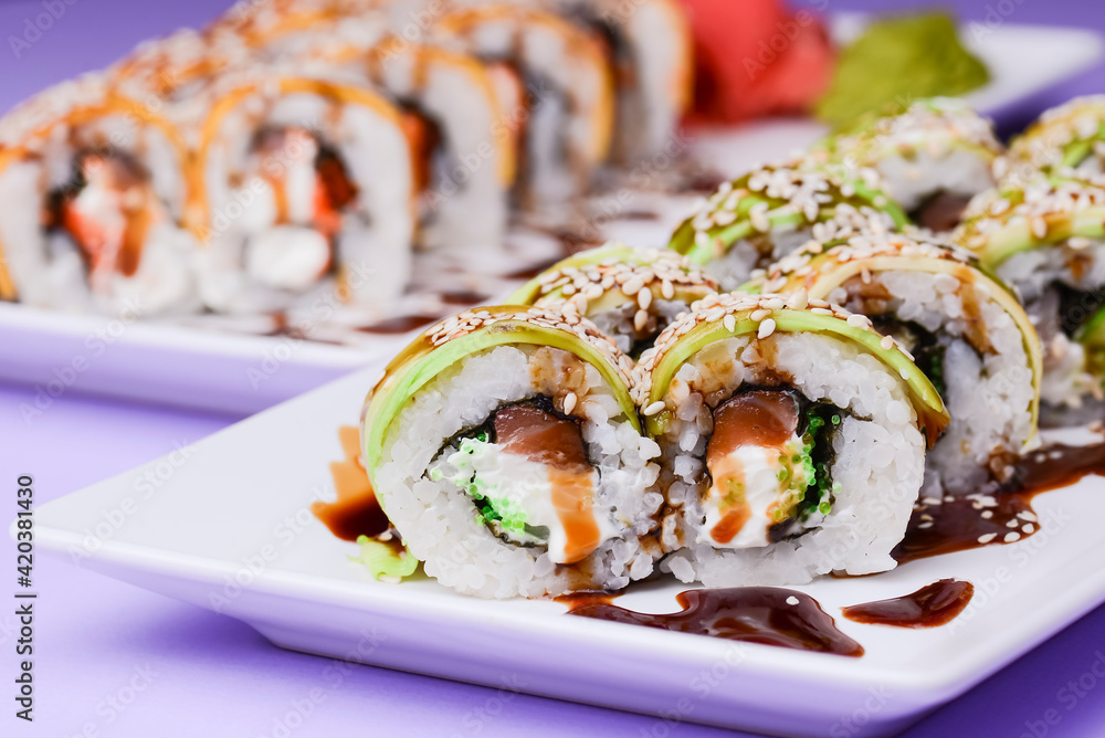 Eel, salmon and tuna sushi with unagi sauce served on a white plate over purple background. Eel, salmon and tuna sushi with unagi sauce served on a white plate over purple background.