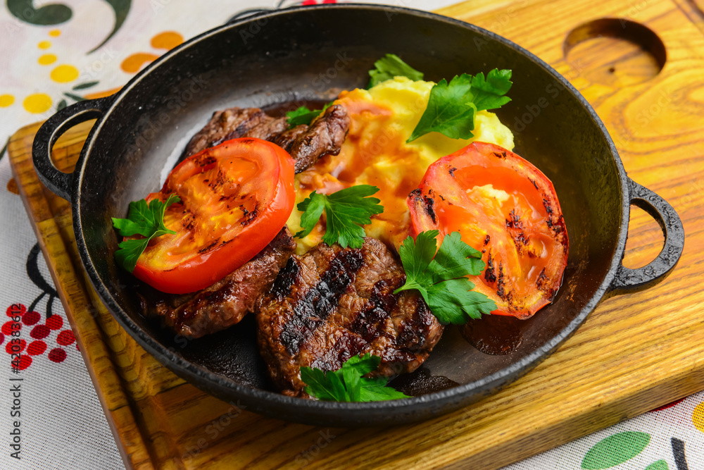 Close up of juicy beef steak served in a pan with bbq grilled tomatoes over traditional Ukrainian tablecloth. Close up of juicy beef steak served in a pan with bbq grilled tomatoes over traditional Ukrainian tablecloth.