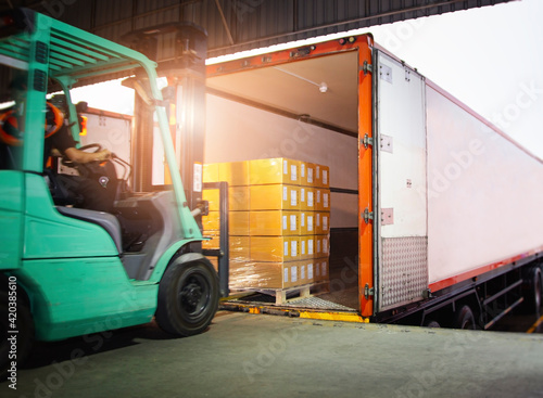 Forklift Tractor Loading Package Boxes into Cargo Container. Cargo Trailer Truck Parked Loading at Dock Warehouse. Shipment Delivery Service. Shipping Warehouse Logistics.  Freight Truck Transport.	
