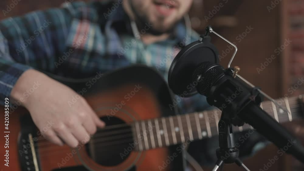 Microphone close-up. Young male musician singing and playing guitar, recording a song at home. Microphone close-up. Young male musician singing and playing guitar, recording a song at home.