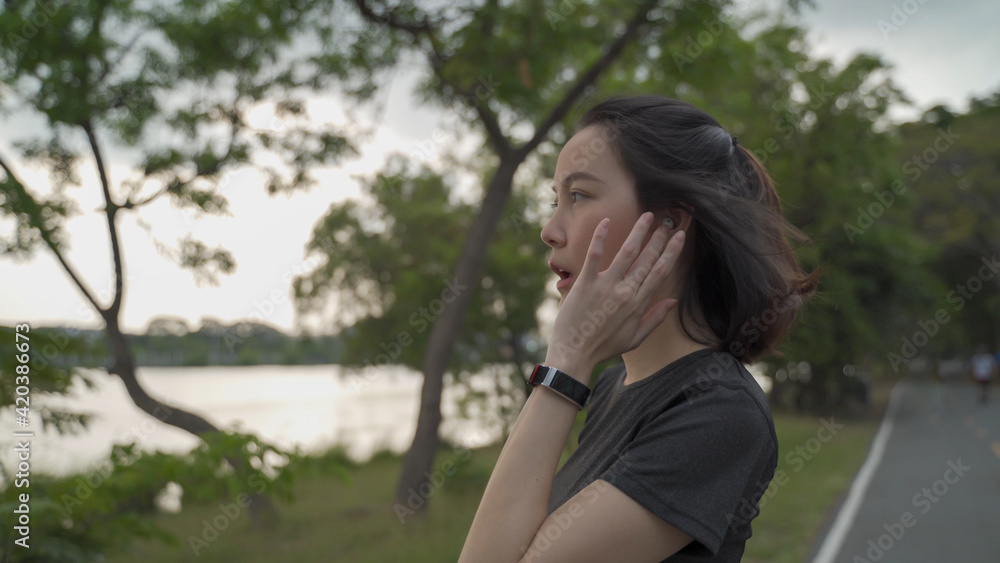 asian sport woman notification from smart watch and answering phone call via wireless earphone at green lake park. female in sportswear talking and hangup phone call by tapping. technology digital. asian sport woman notification from smart watch and answering phone call via wireless earphone at green lake park. female in sportswear talking and hangup phone call by tapping. technology digital.
