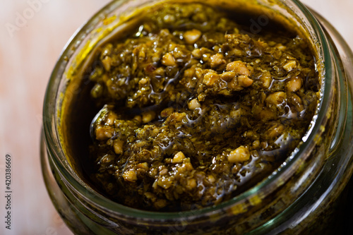 Closeup of organic pesto sauce in glass jar on wooden surface