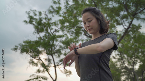 asian athlete woman using sport smart watch green nature park in evening sunset. female in sportswear touching screen application tracking activity and music. enjoy personal record data performance. © Vajirawich