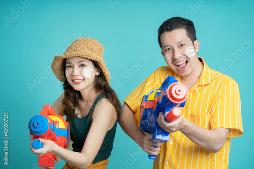 Asian couple holding plastic water guns happy for Songkran festival, isolated on blue background.