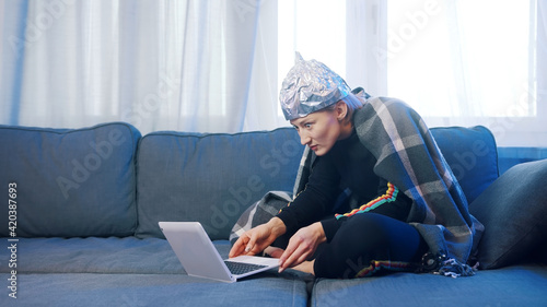 Fearful young woman with aluminum hat browsing social media. Conspiracy theory about 5g network destroying brain. High quality photo