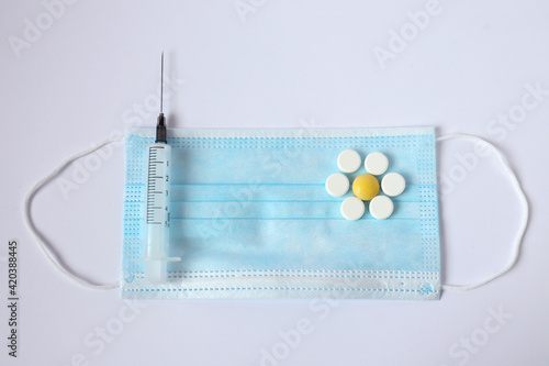 Chamomile from tablets on a medical mask, syringe, white background, top view-the concept of a good treatment result