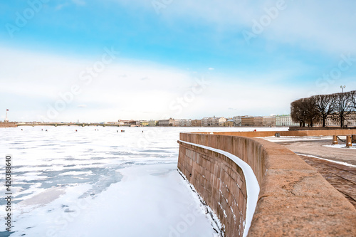 View of the Hermitage  Winter Palace  from the embankment of St. Petersburg from the icy Neva River  people walk along the river in early spring