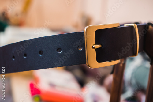 Blue leather belt with gold buckle against the background of the leather master's workplace